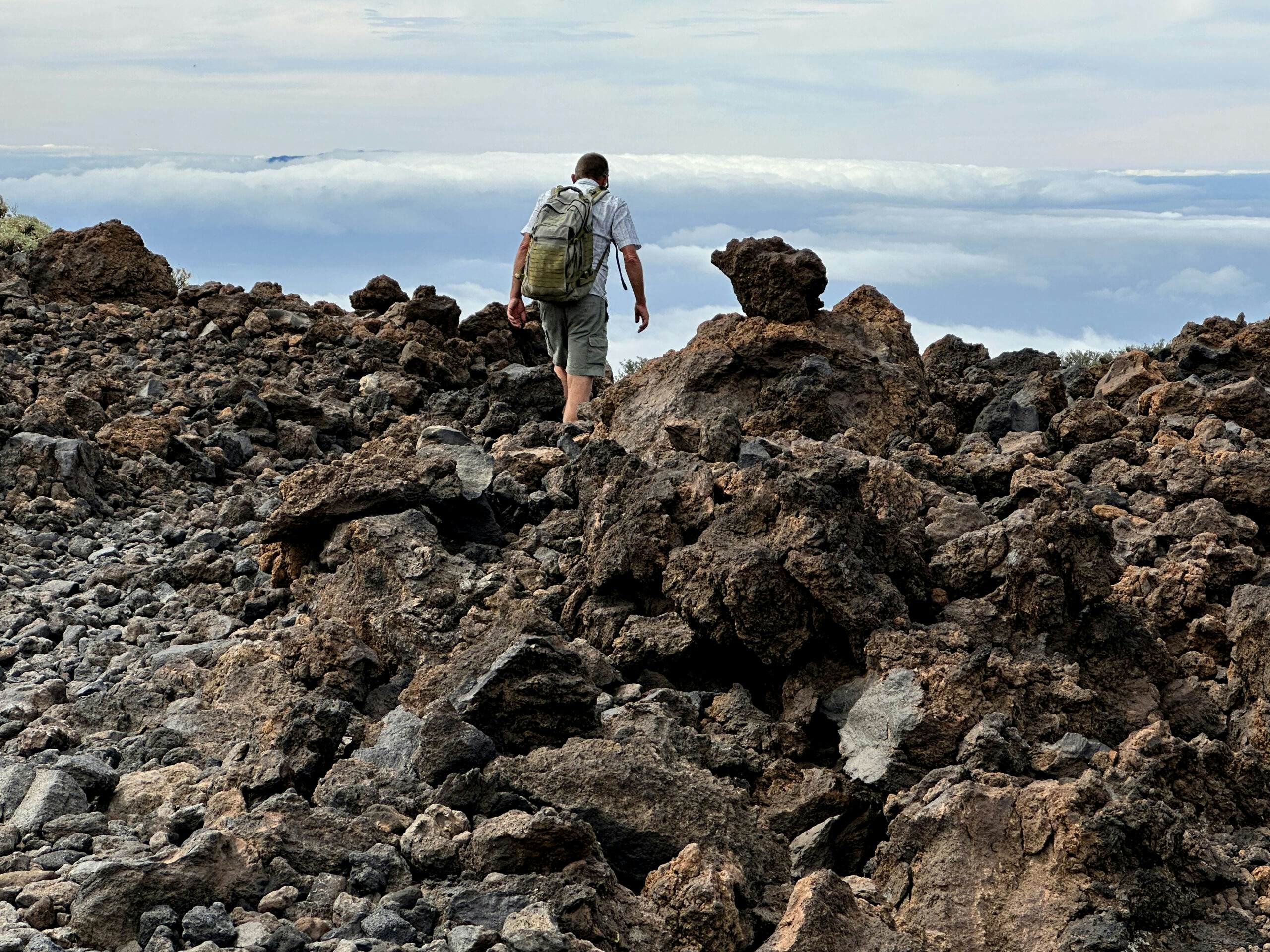 Senderista en el sendero a través de roca volcánica por encima de las nubes
