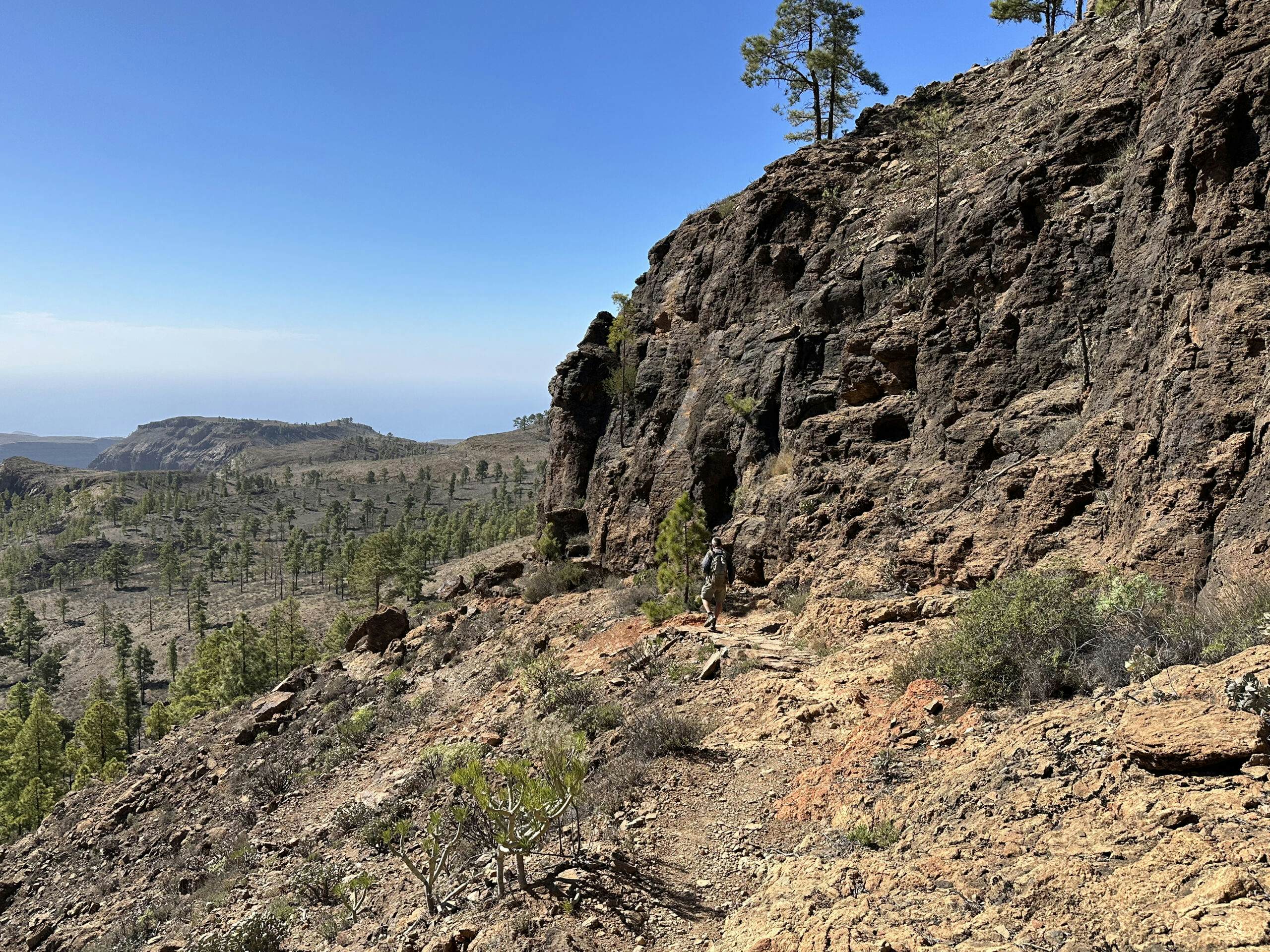 Hiker on the hiking trail below Montaña Tauro and the rock face with the caves