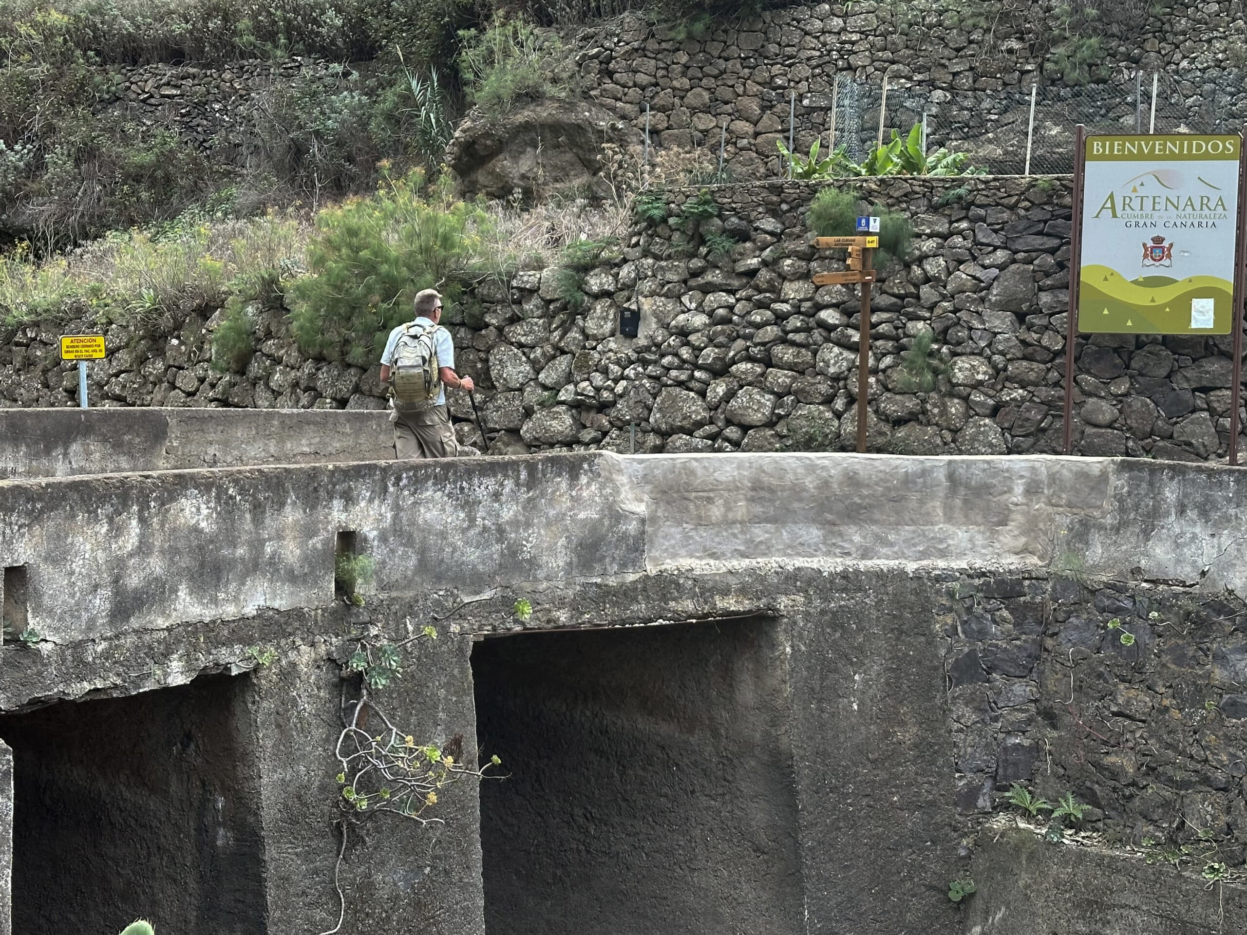 Hiker on the bridge at the Presa de los Perez reservoir - the GR-138 hiking trail branches off to the left, which was closed at Risco Caído in December 2024