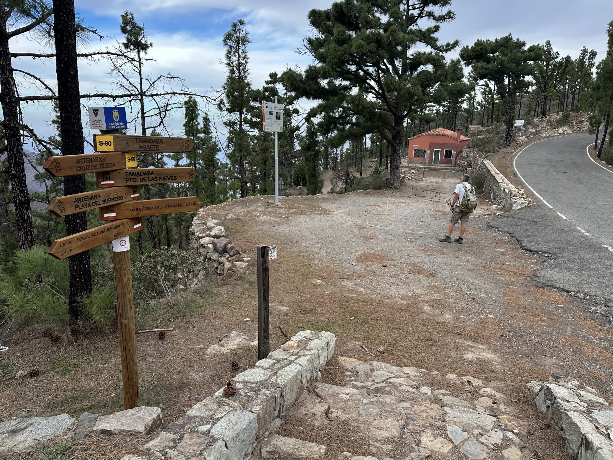 Hiker on the hiking trail in front of the red house (Casa Roja de Tirma) at the Degollada Honda on the GC-216 at the beginning of the Tamadaba nature reserve