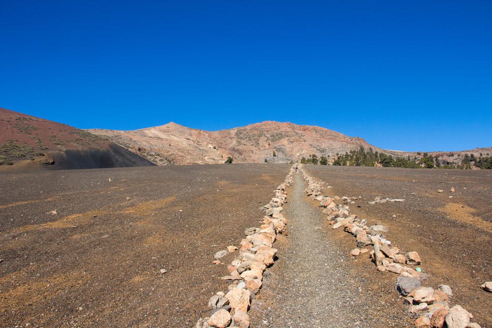 Ruta de senderismo recta marcada con hileras de piedras en un extraño paisaje arenoso