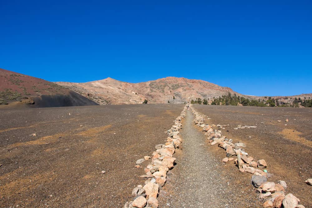 Ruta de senderismo recta marcada con hileras de piedras en un extraño paisaje arenoso