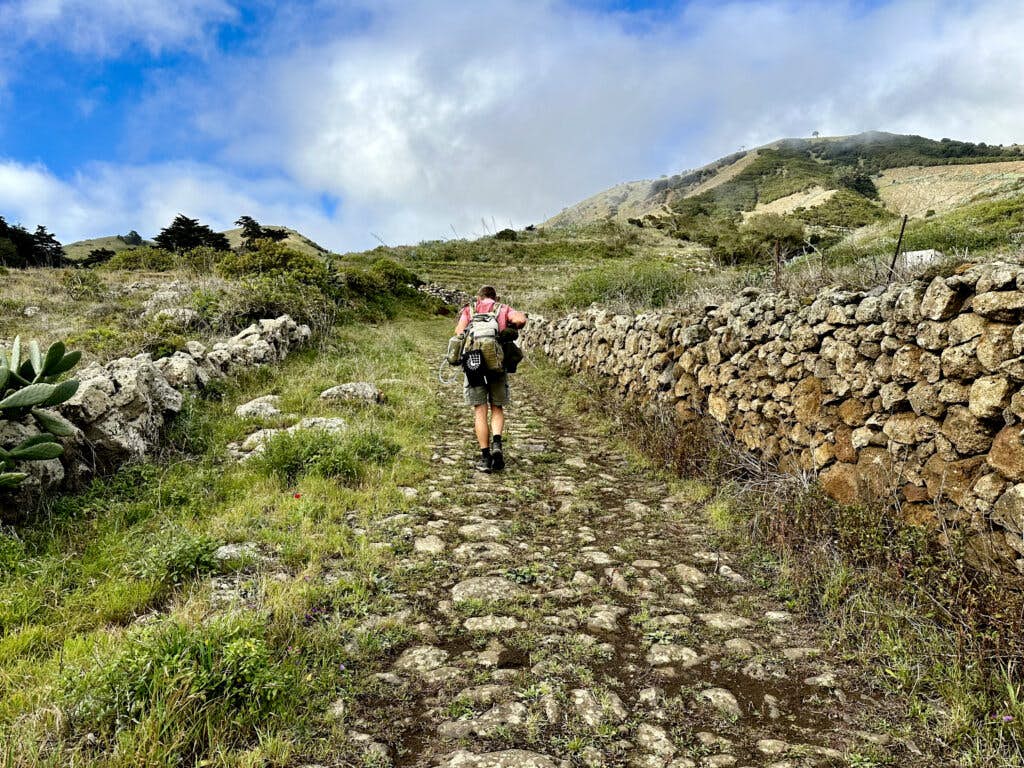 Senderista en el sendero de larga distancia GR-131 Camino de la Virgen de El Hierro, cerca de San Andrés - sendero con muros de piedra
